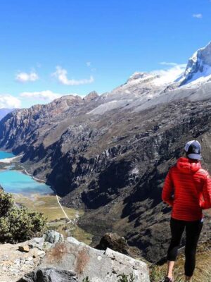 Person in a red jacket overlooking a valley with turquoise lakes and snow-capped mountains on the Santa Cruz Trek