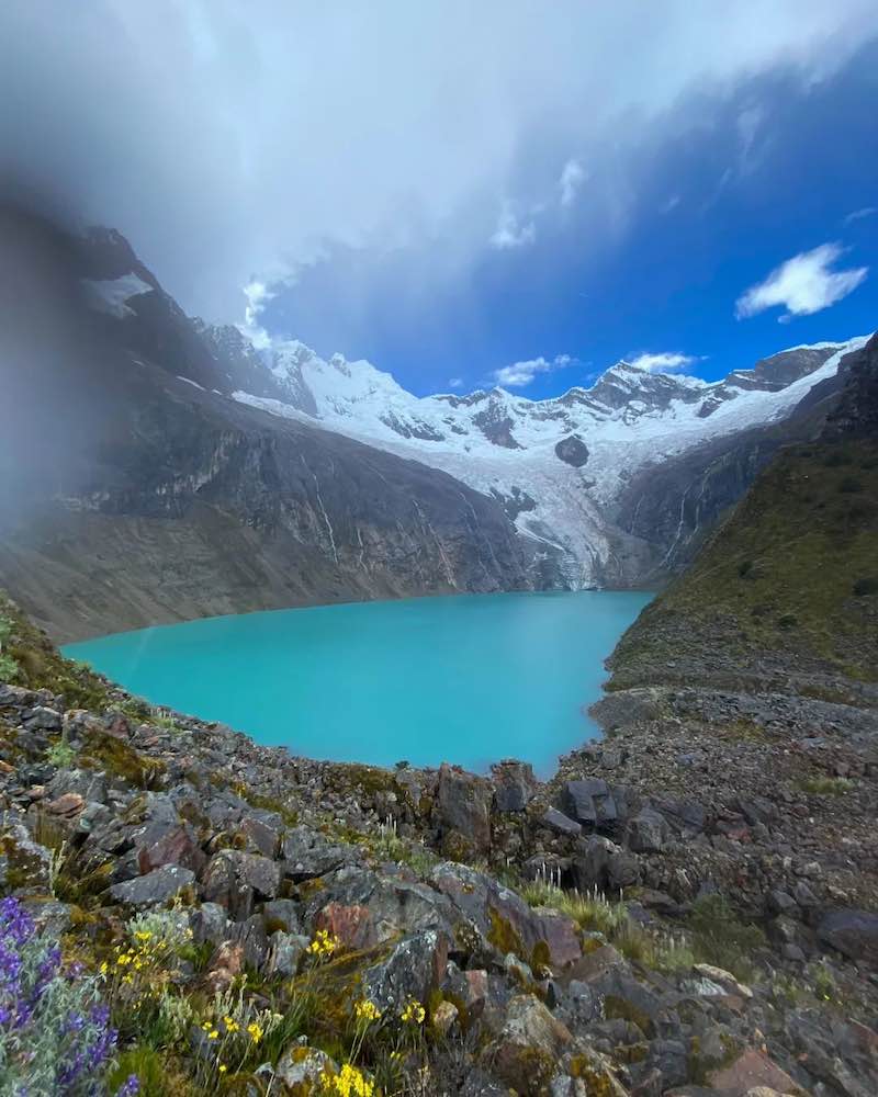 Turquoise lake surrounded by rocky mountains and snow-capped peaks under a cloudy sky on the Santa Cruz Trek